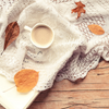 Leaves and hot chocolate in white teacup over white blanket on hardwood