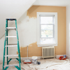 Green ladder leaning against partially painted beige wall in white renovated room with drop cloth and tools on ground