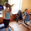 Caucasian couple working out at home. Woman on the treadmill watching TV and the man sitting on a free weight bench doing arm curls
