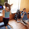 Home Gym Blog 1 Caucasian couple working out at home. Woman on the treadmill watching TV and the man sitting on a free weight bench doing arm curls