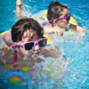 Little girls thumbnail Two girls with brown hair and sunglasses swimming in pool with floaty ring. Square photo