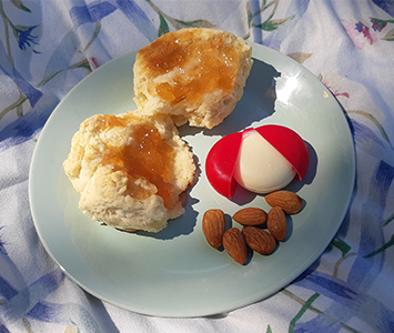 A plate with jam on a scone or biscuit, a few almonds and a small cheese.