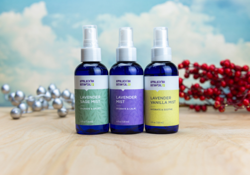 three bottles of Appalachian Botanical Co. mist - lavender safe, lavender and lavender vanilla on hardwood floor with silver and red decor in background