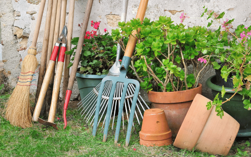 Garden tools leaning against some flower pots and a stone backyard wall 