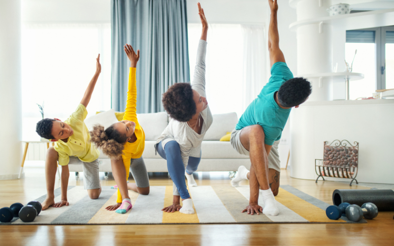 family of four in side lunch yoga pose with left arm reaching to the ceiling working out as a family, GYM MEMBERSHIP OR HOME GYM? IN 2023