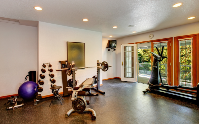 Home gym with purple pilates ball, free weight rack, treadmill, and TV with motivational poster on wall. Patio doors open wide