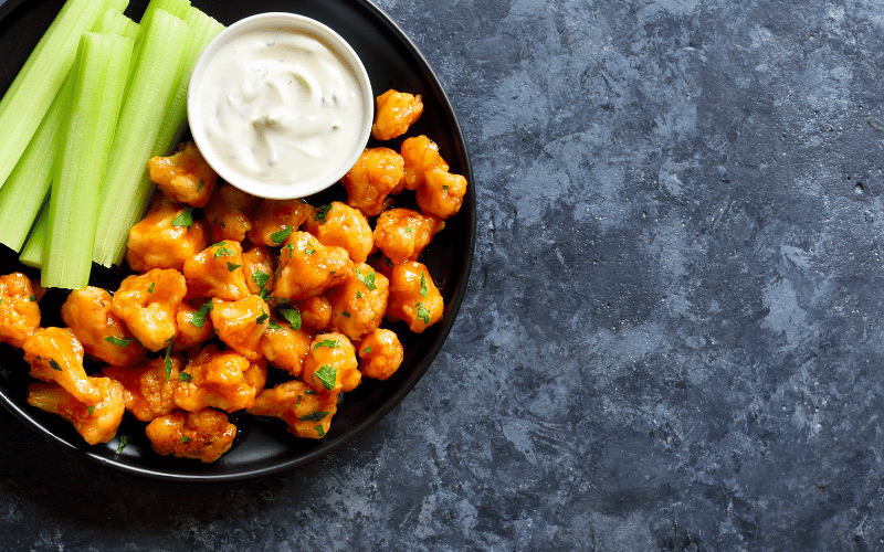 Blue granite counter with black plate full of buffalo cauliflower wings celery and blue cheese dip.