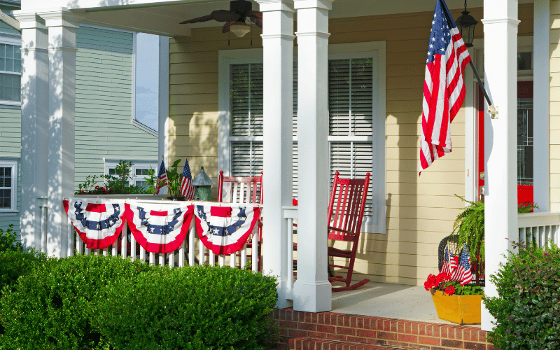 Front porch with white beams and yellow shutters decorated with US decoration for Independence Day