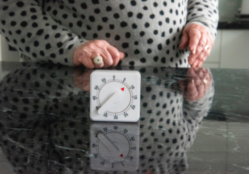 Woman wearing grey sweater with black polka dots stands beside kitchen timer on black granite countertop