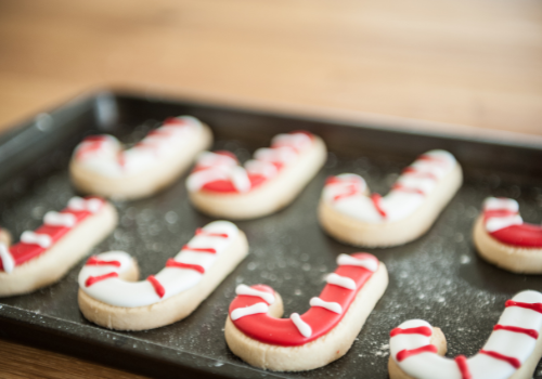 Tray of 8 candy cane shaped iced sugar cookies on baking pan with red and white striped icing