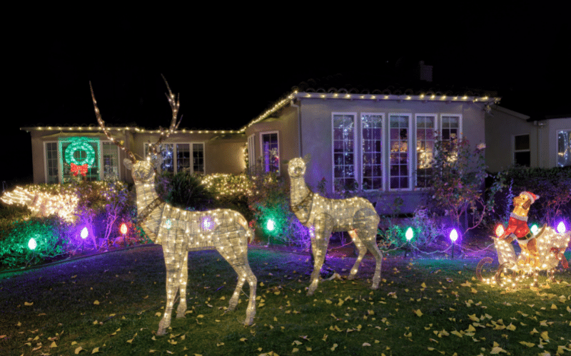 Outdoor Christmas decorating with light up reindeer, Santa sleigh, green wreath in window and white lights along eavestrough