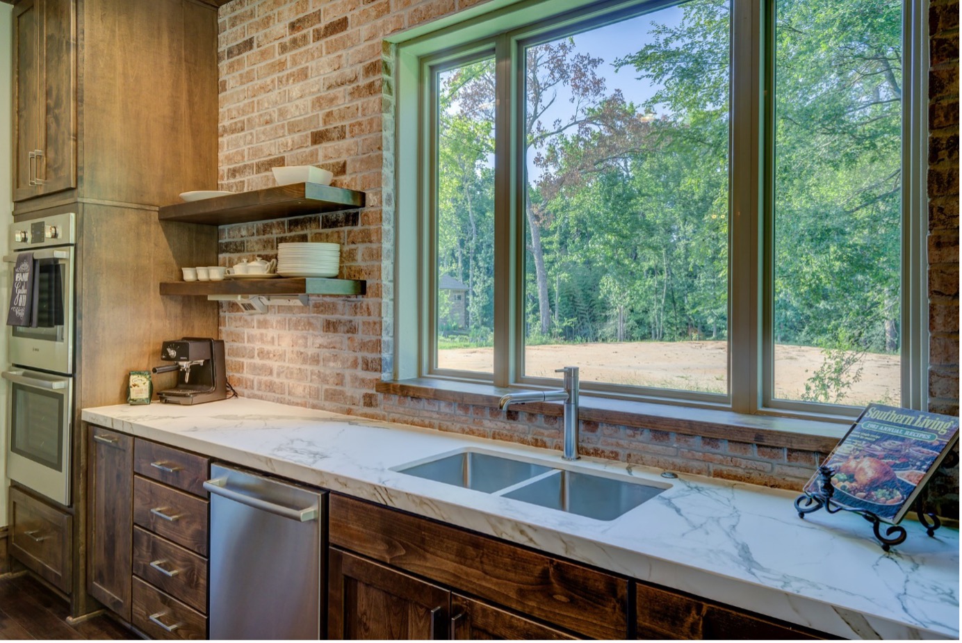 modern dark wood brushed lower cabinets with fresh white marble countertops and brand new stainless kitchen faucet and sink overlooking large field in backyard through large rectangular window