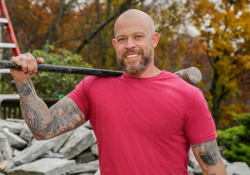 HGTV Joe Mazza wearing a red T-shirt smiling and holding a sledgehammer over his shoulder in his right hand