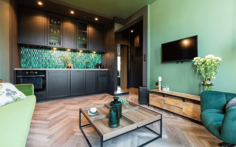 green themed room with green walls matching couch and a dark green luxury chair, a small wooden low table and a dark green kitchen backsplash 