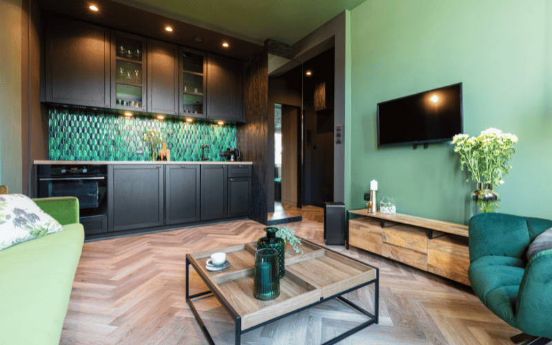 green themed room with green walls matching couch and a dark green luxury chair, a small wooden low table and a dark green kitchen backsplash