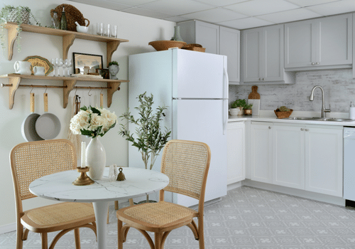 white kitchen with freshly painted cabinets. Flowers in white vase on table next to hanging pots and floor plant beside white fridge