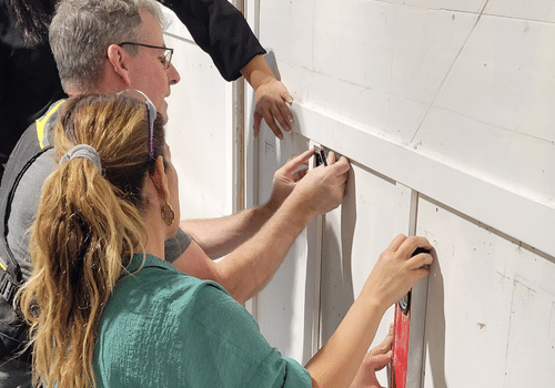 Older man and younger woman working together measuring something with a helping hand on a white wall