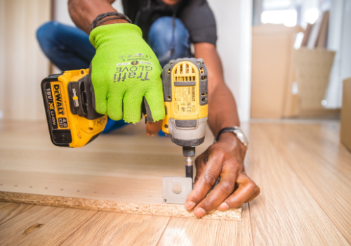 Contractor using power drill to install corner bracket on wood, wearing neon green glove and watch on left arm