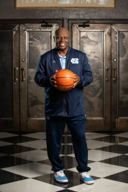 Basketball star Phil Ford holds a basketball in UNC coach's uniform