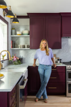 Designer Tamara Day stands in a kitchen she designed with mulberry cabinets and gold hardware